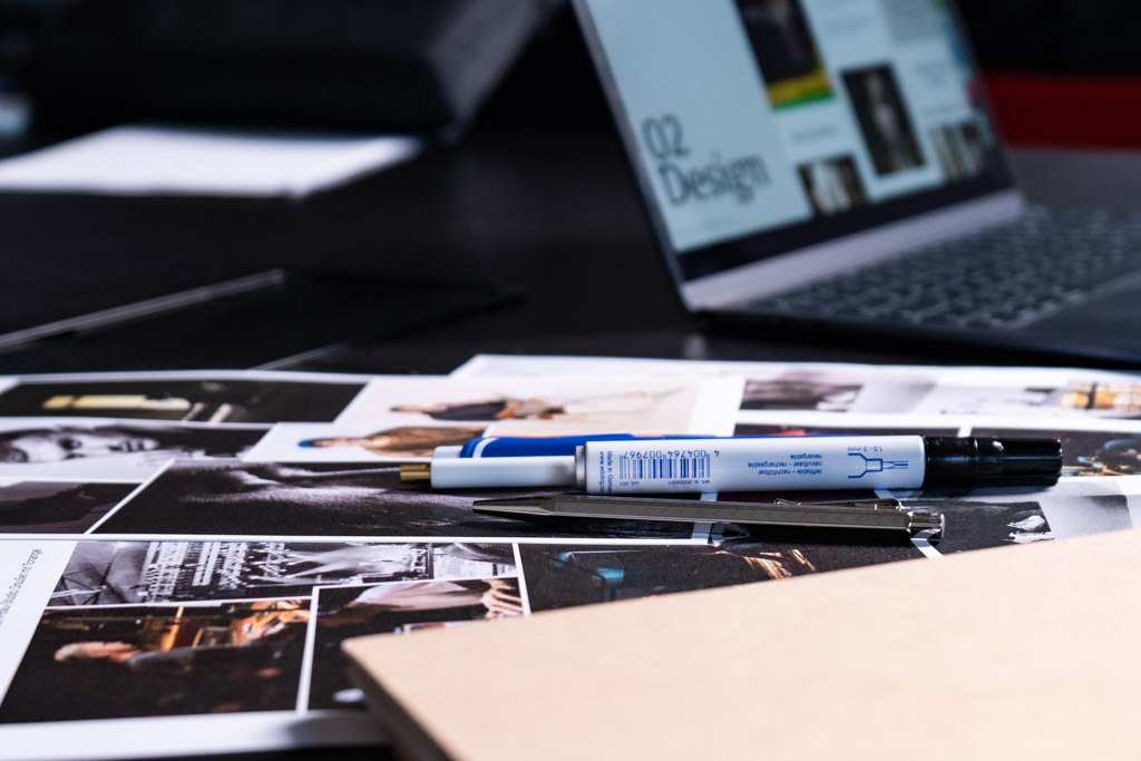 Eine Nahaufnahme von Stiften, Designunterlagen und eines Macbooks.