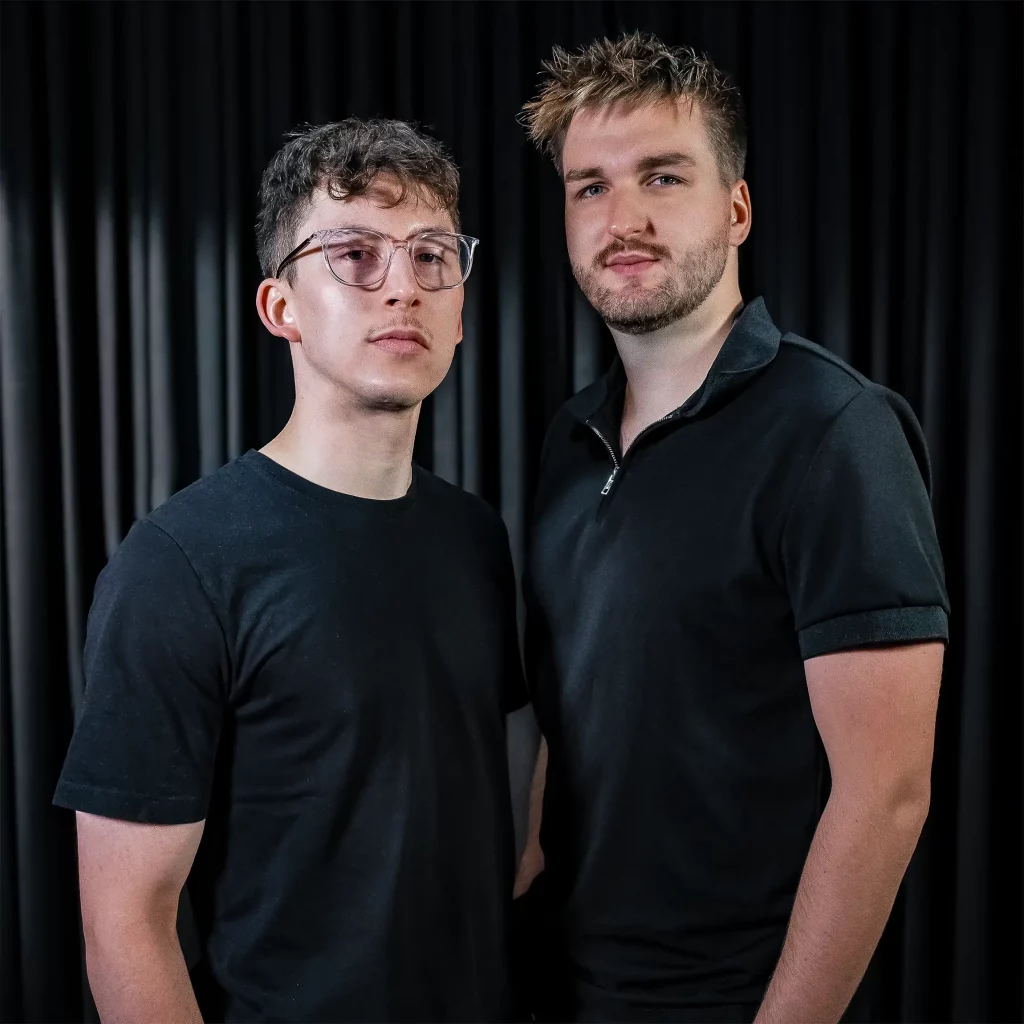 Fabian und David stehen vor einem schwarzen Vorhang und schauen in die Kamera.