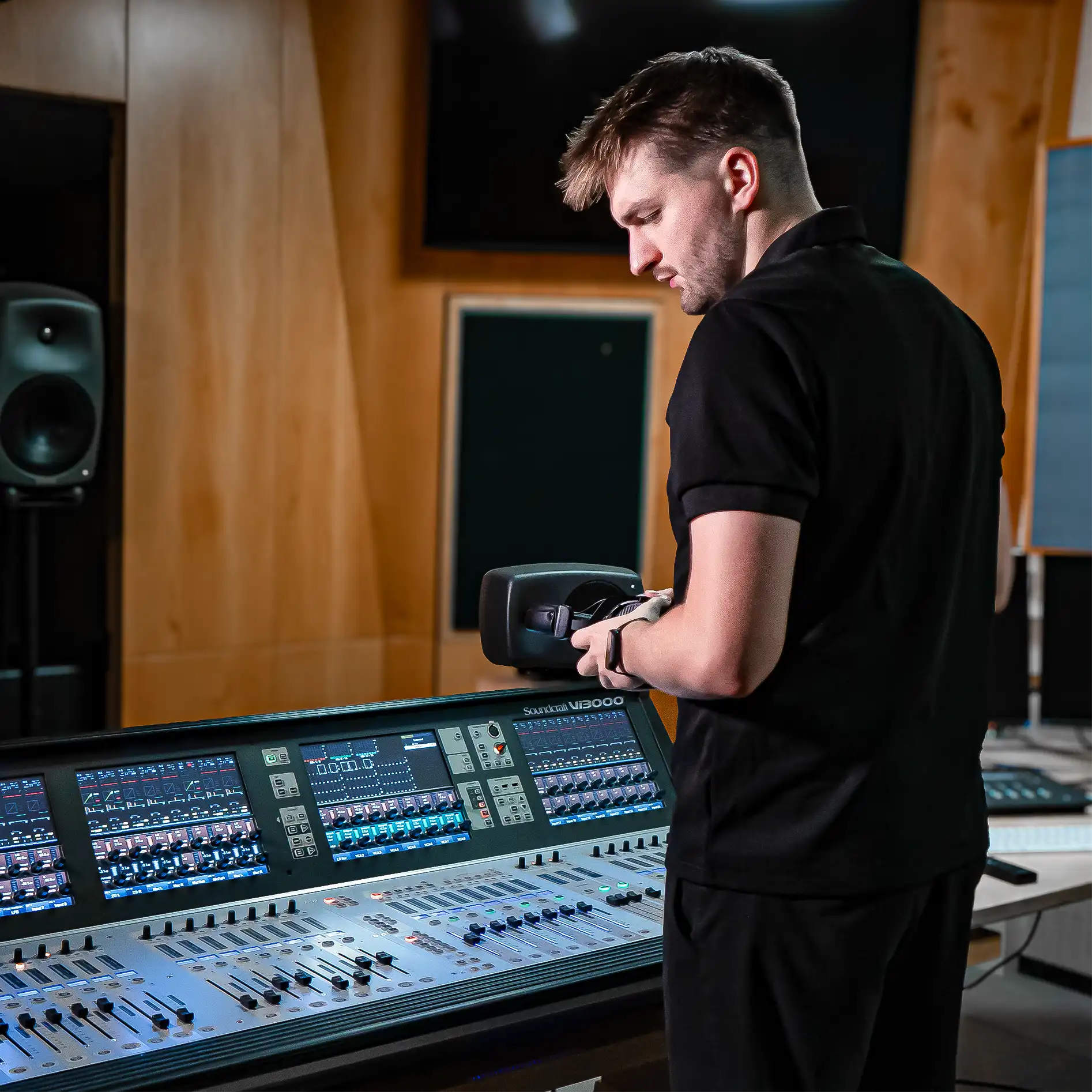 David steht vor einem Mischpult mit Kopfhörern in den Händen.
